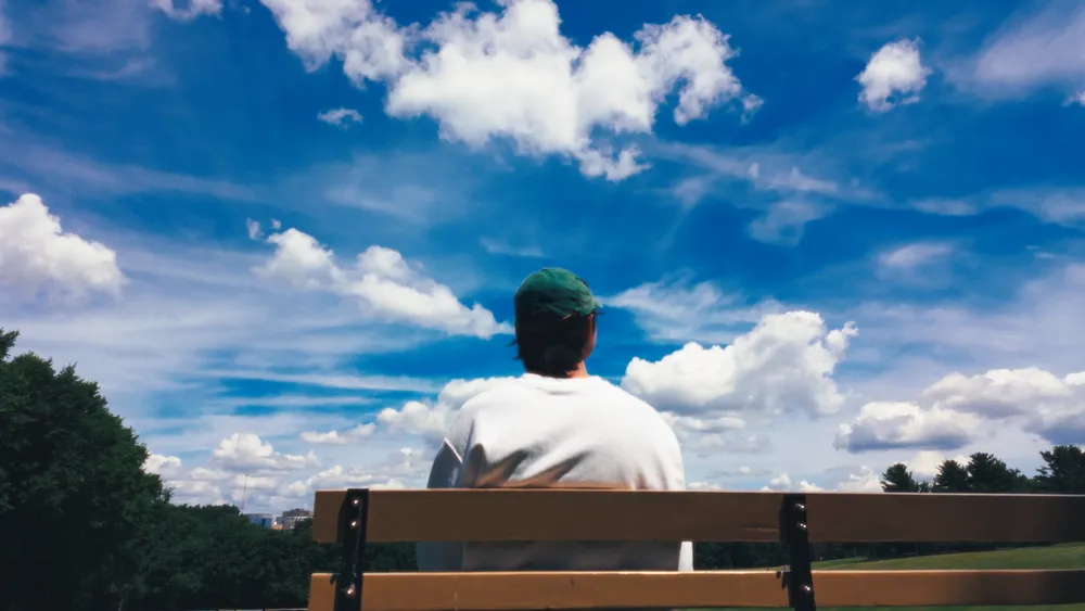 Ben sitting beneath a sky full of clouds, a frame from his films